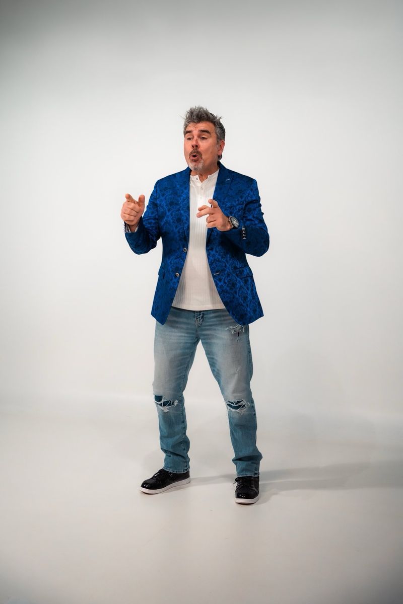 Tristan Alexander in a blue paisley blazer, smiling and pointing toward the camera