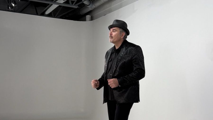 Tristan in a black sparkling jacket and fedora, striking a classic crooner pose