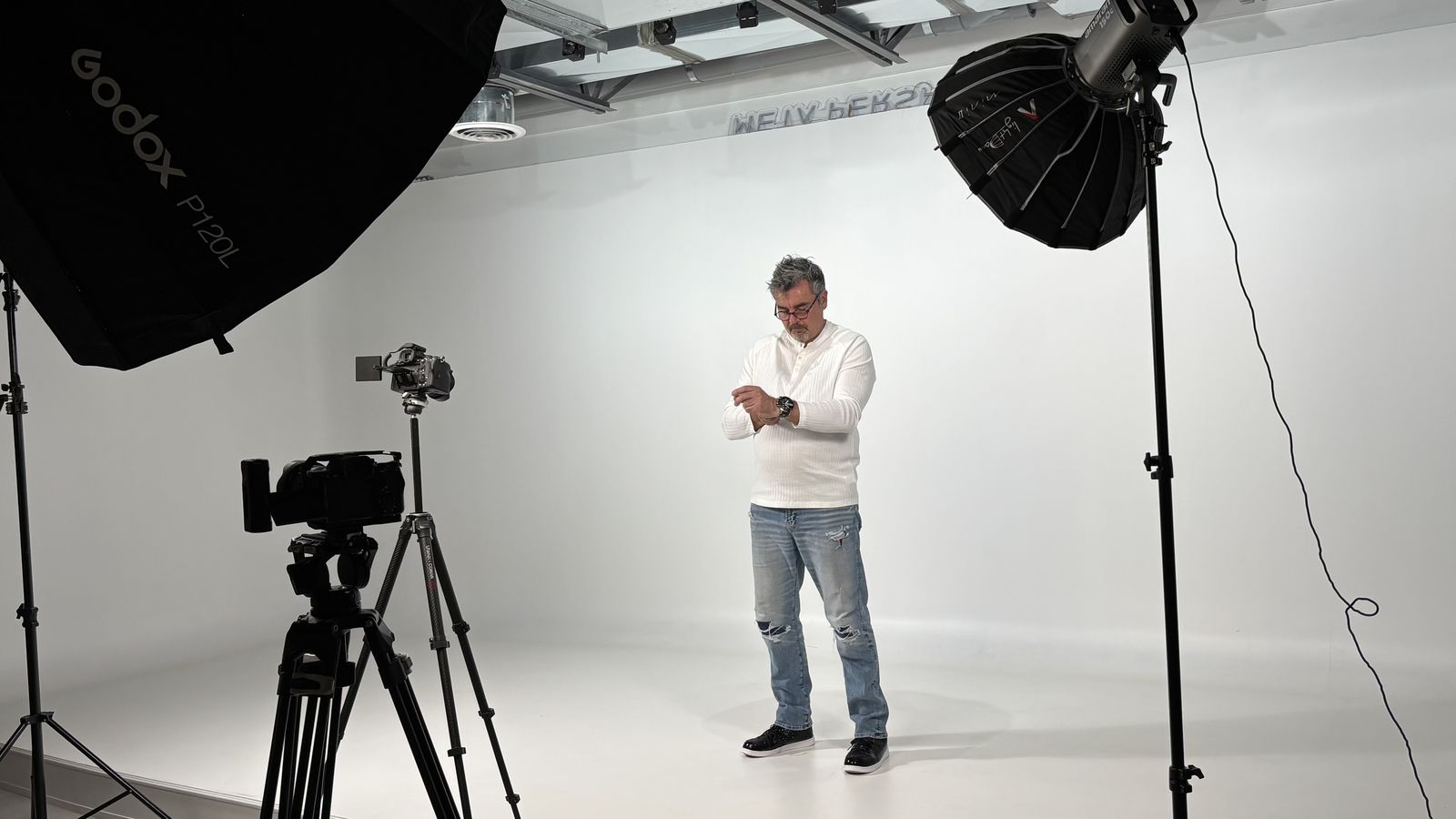 Behind the scenes: Tristan in a white sweater on a studio set surrounded by lights and cameras