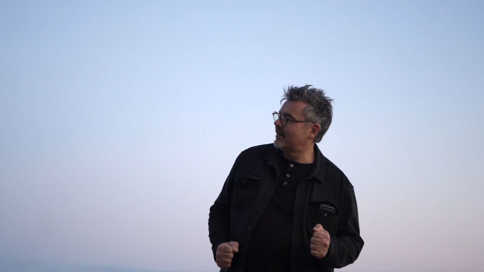 Tristan in a black jacket against a pastel dusk sky, moving to the beat